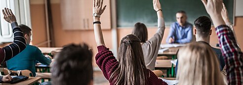 High school students raise their hands in class.