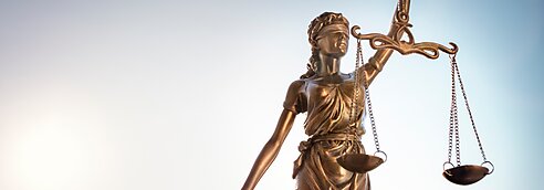 Lady justice holding scales against a pale background