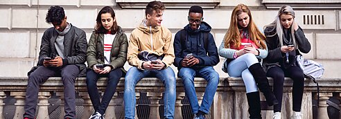 Teenagers sitting on top of a wall looking at their phones