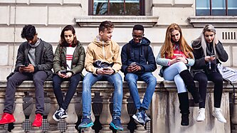 Teenagers sitting on top of a wall looking at their phones